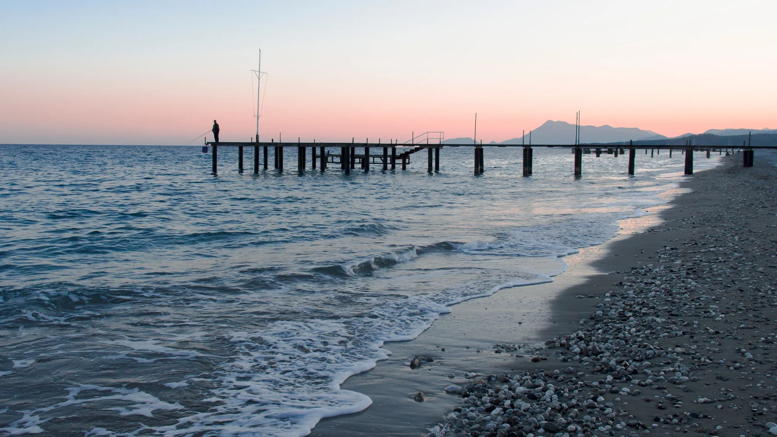 Sunset over Kiriş Beach with a pier and the Taurus Mountains in silhouette